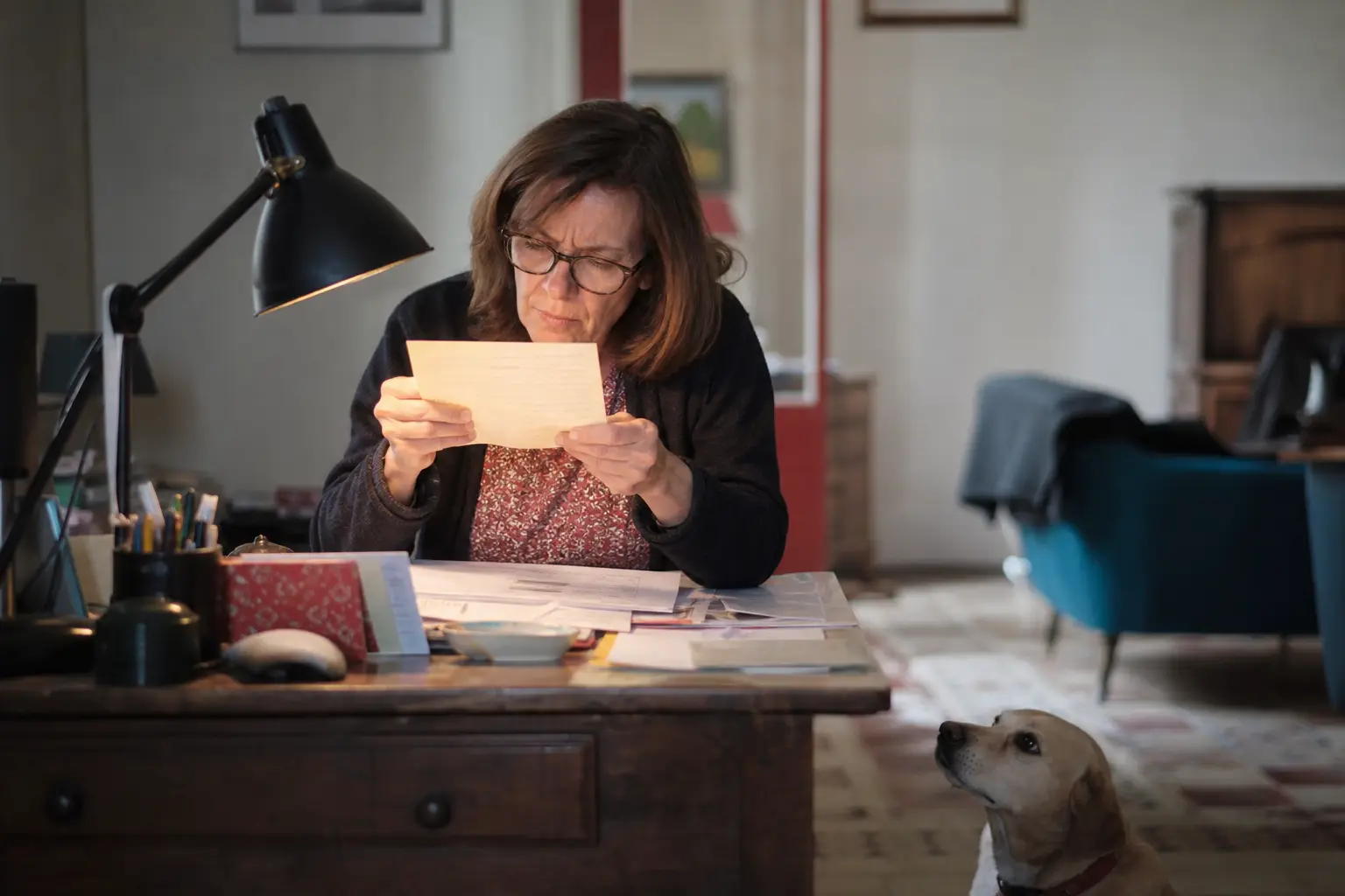 Femme lisant les petites lignes d'un document près de sa lampe de bureau, son chien la regardant depuis le sol